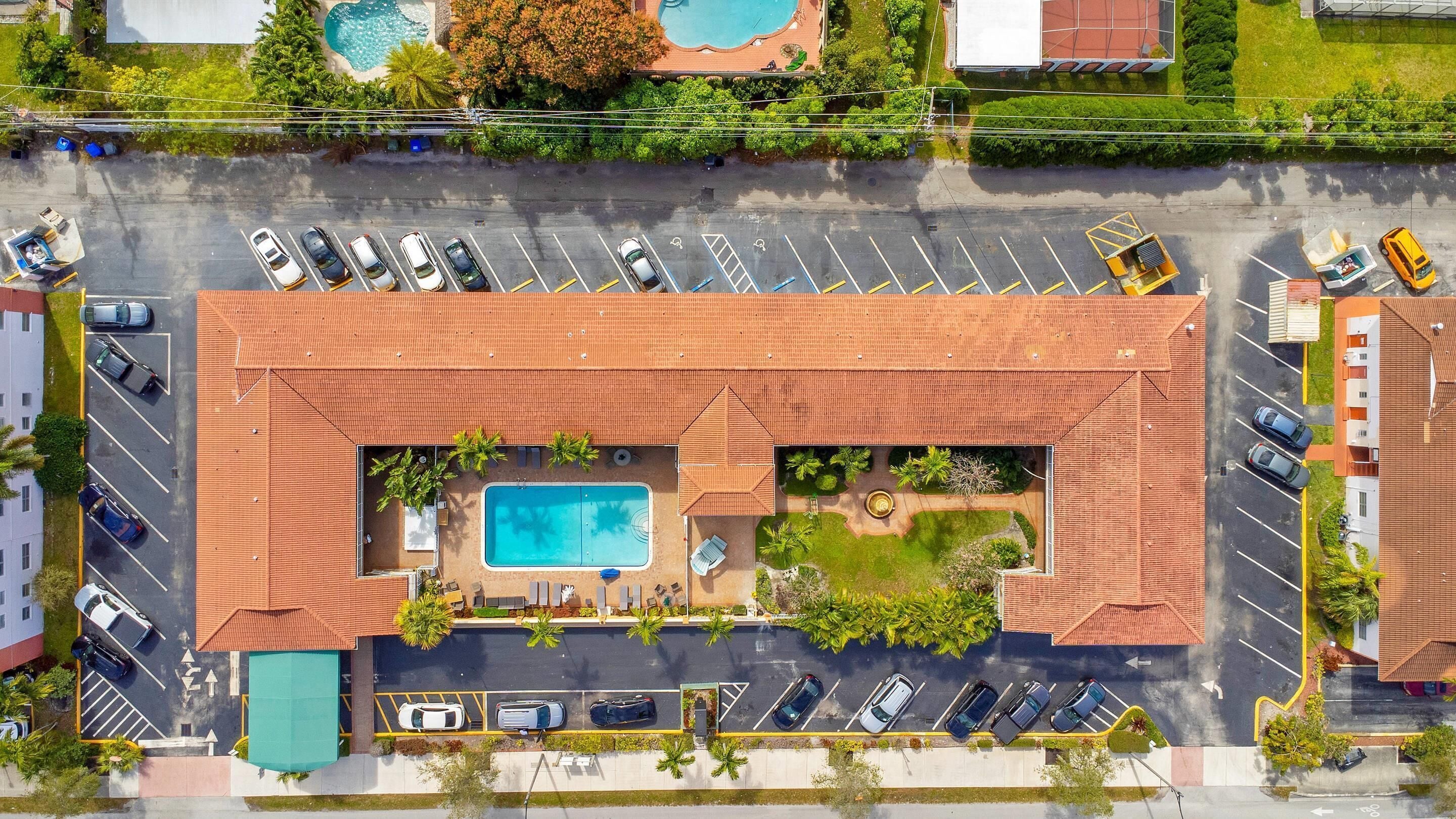 An aerial view of a hotel with a swimming pool, parking lot, and adjacent buildings.