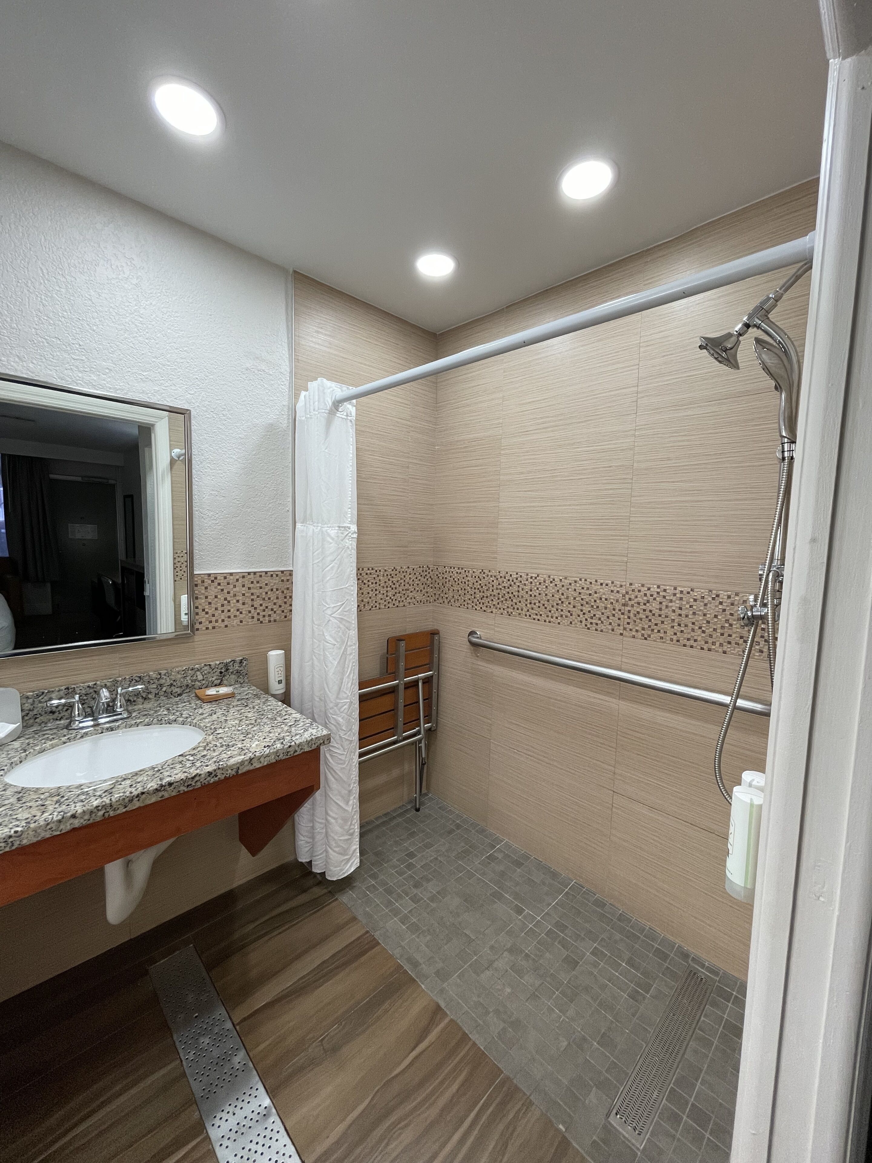 A bathroom with a sink, mirror, shower, and grab bar.