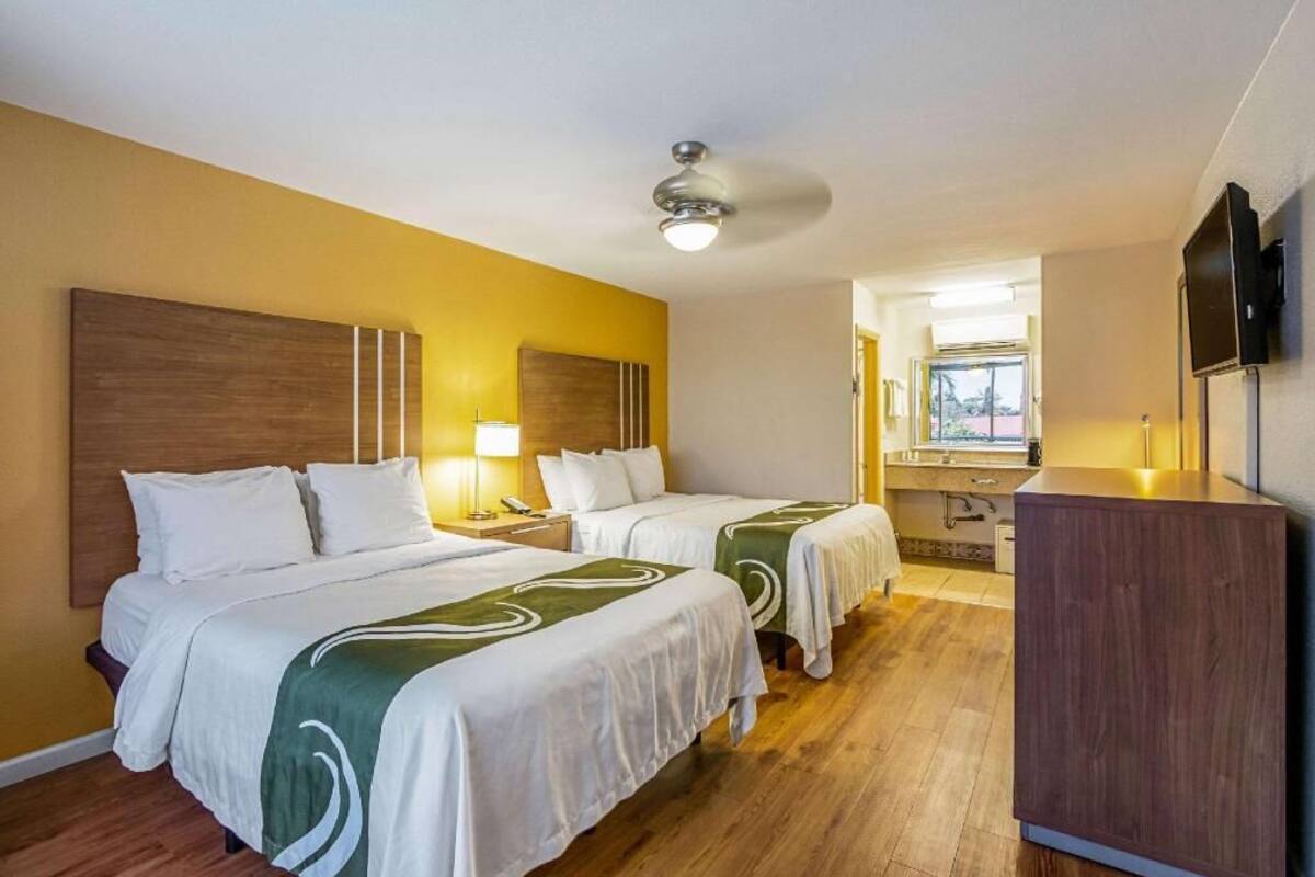 Een hotelkamer met twee bedden, een houten hoofdbord, een bureau met stoel, een televisie en een raam.