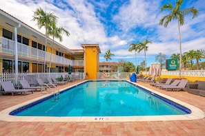 Uma área de piscina de hotel com uma piscina azul cristalina, espreguiçadeiras e palmeiras.
