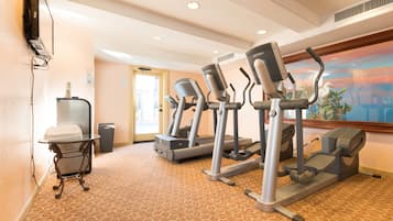 A hotel fitness room with treadmills, a small table with towels, and a painting on the wall.