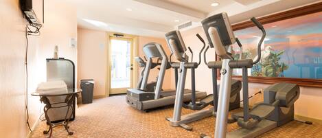 Et hotel fitnessrum med løbebånd, et lille bord med håndklæder og et billede på væggen.