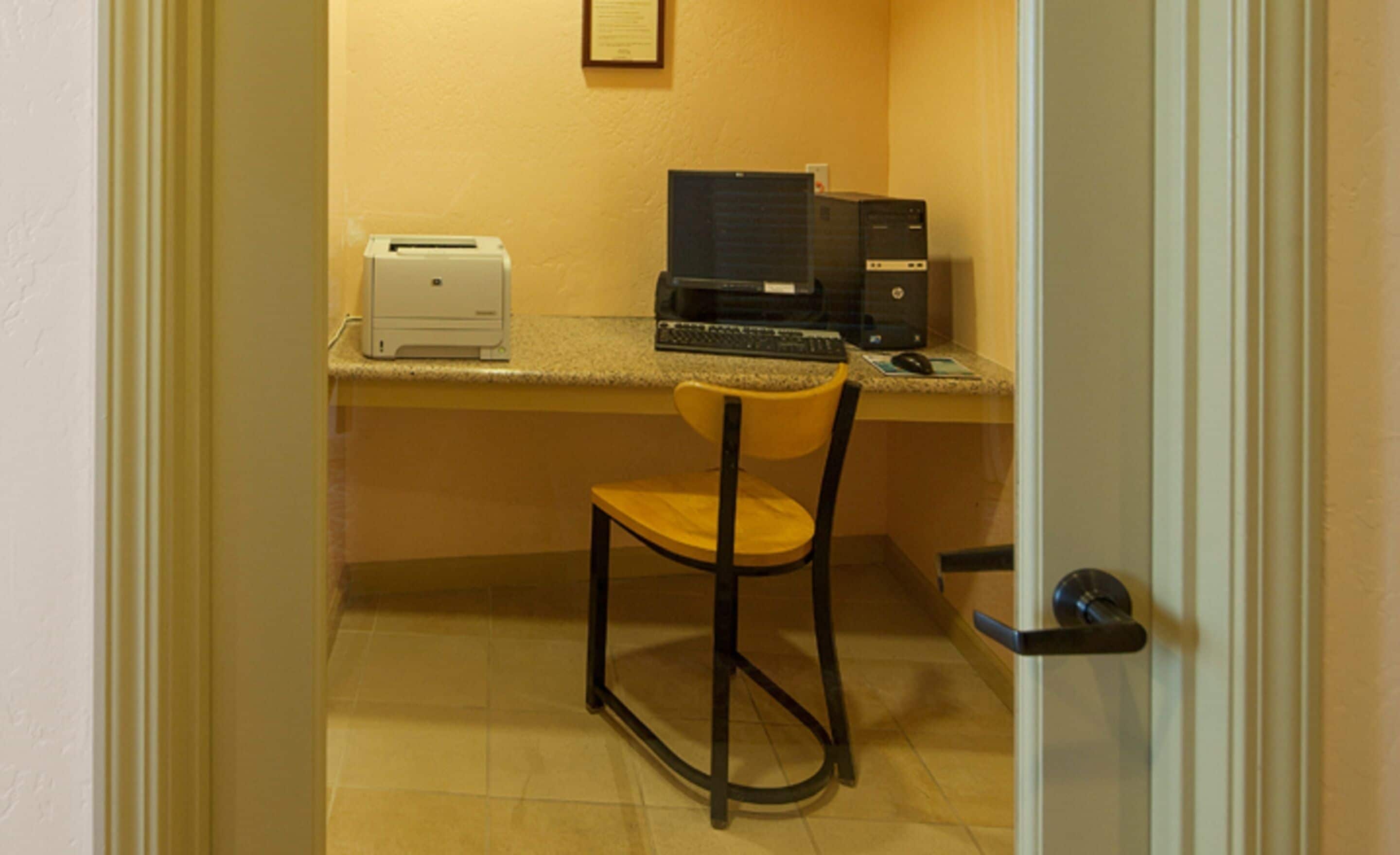 A small office with a desk, a chair, a printer, and a computer.