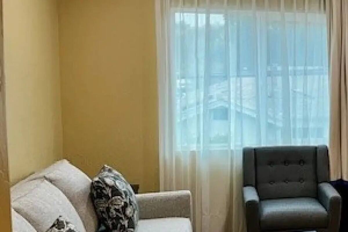 A hotel room with a grey armchair, a sofa, a television mounted on the wall, and a microwave on a wooden table.