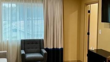 Una habitación de hotel con un sillón gris, un sofá, un televisor montado en la pared y un microondas sobre una mesa de madera.
