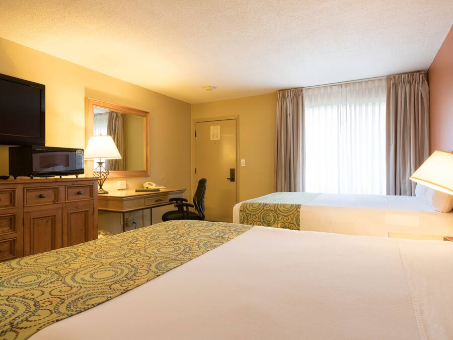 A hotel room with two beds, a desk with a lamp, a television, and a window with curtains.