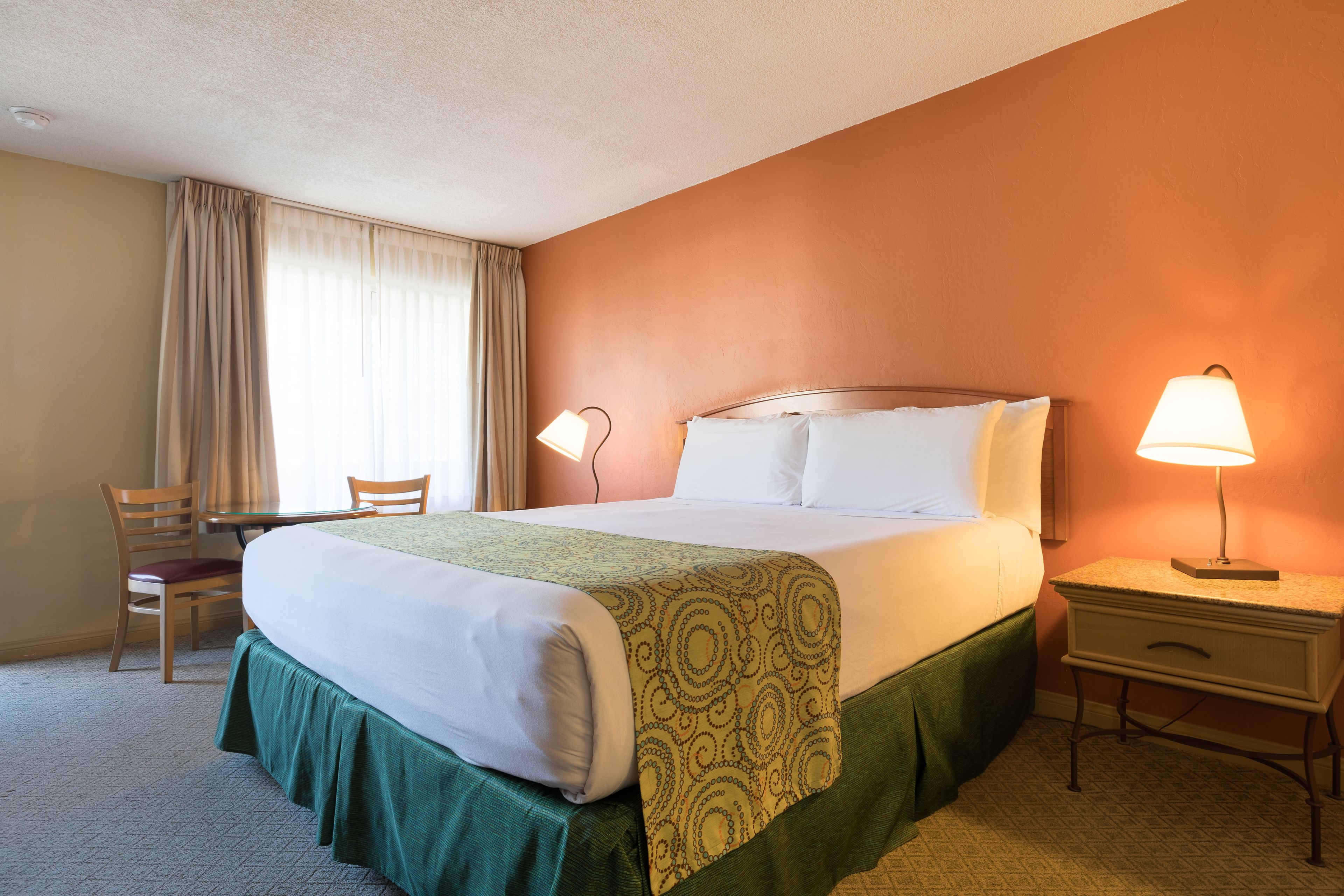 A hotel room with a bed, two bedside lamps, a chair, and a desk.