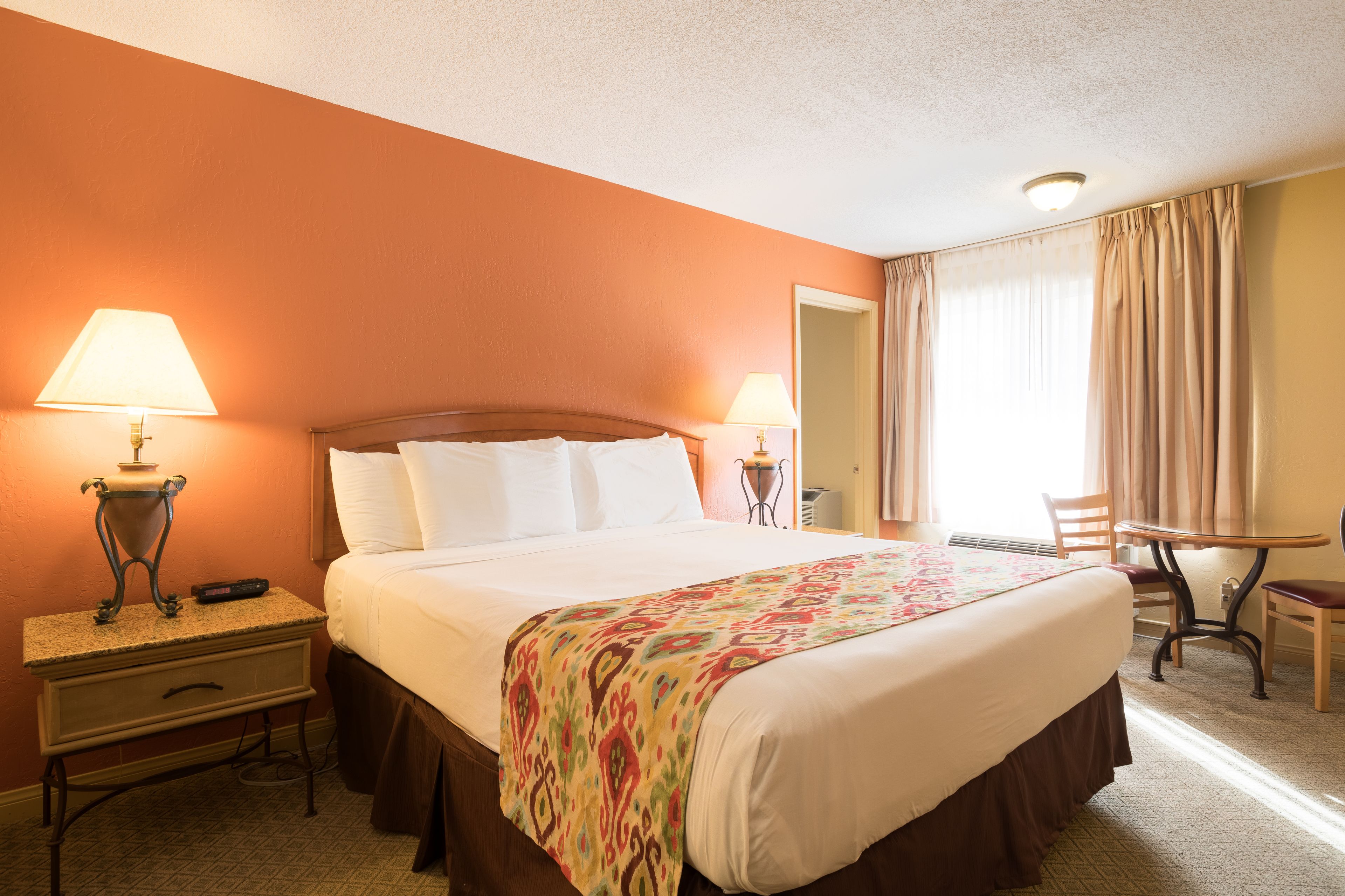 Ein Hotelzimmer mit einem großen Bett, zwei Nachttischlampen, einem Schreibtisch mit Stuhl und einem fenster mit Vorhängen.