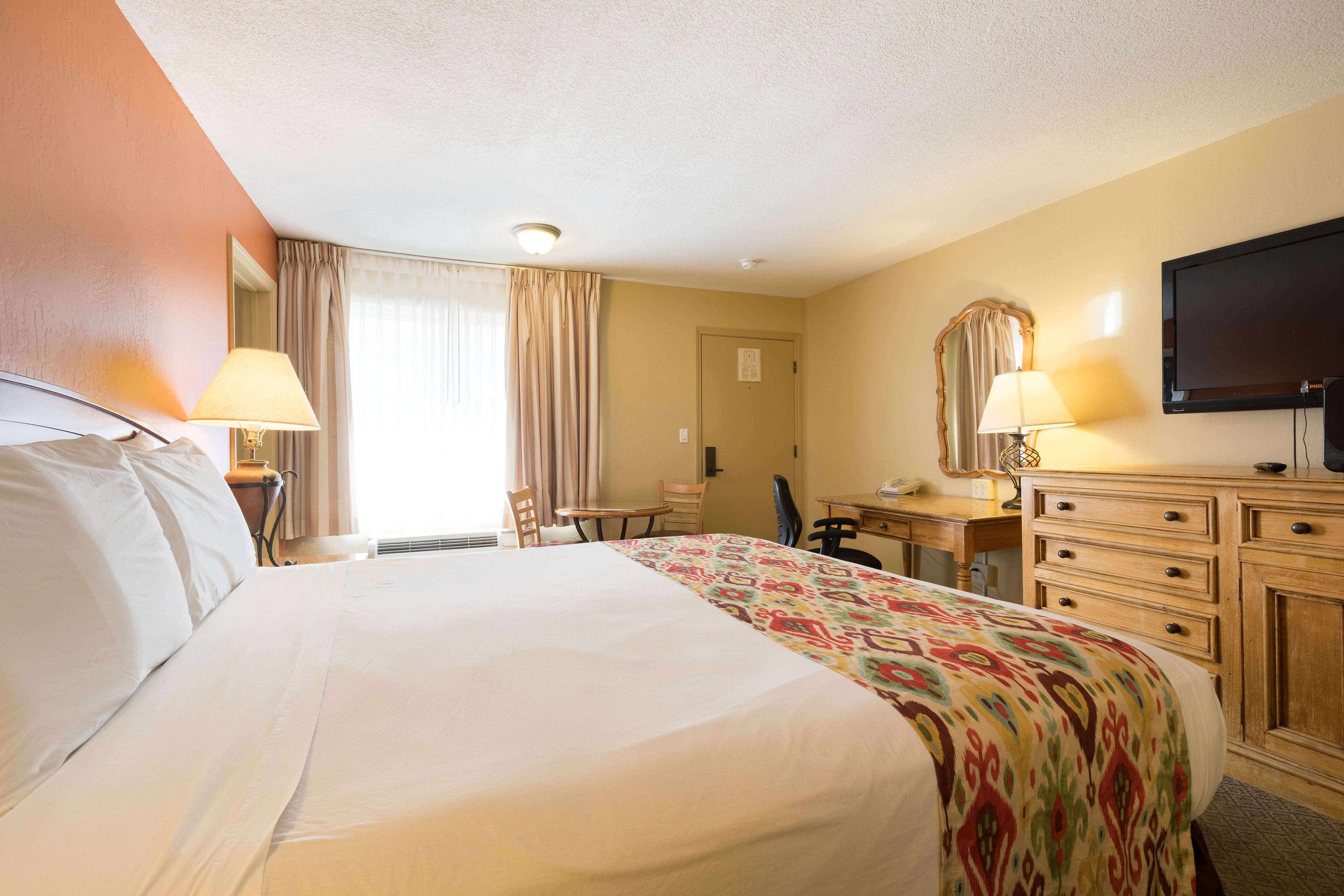A hotel room with a large bed, a desk with a chair, a television, and a dresser.