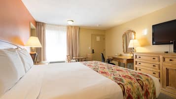 A hotel room with a large bed, a desk with a chair, a television, and a dresser.
