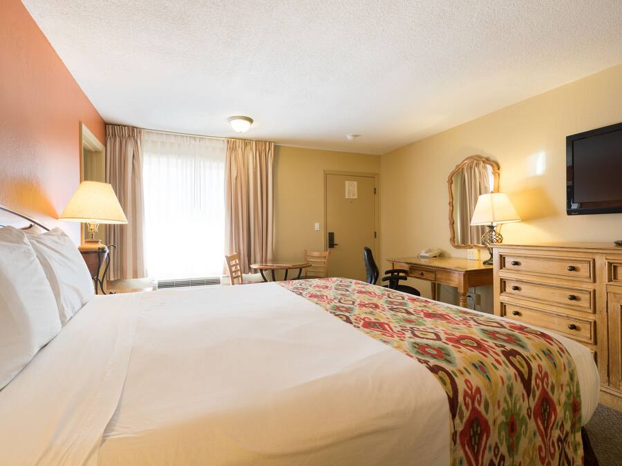 Ein Hotelzimmer mit einem großen Bett, einem Schreibtisch mit Stuhl, einem Fernseher und einer Kommode.