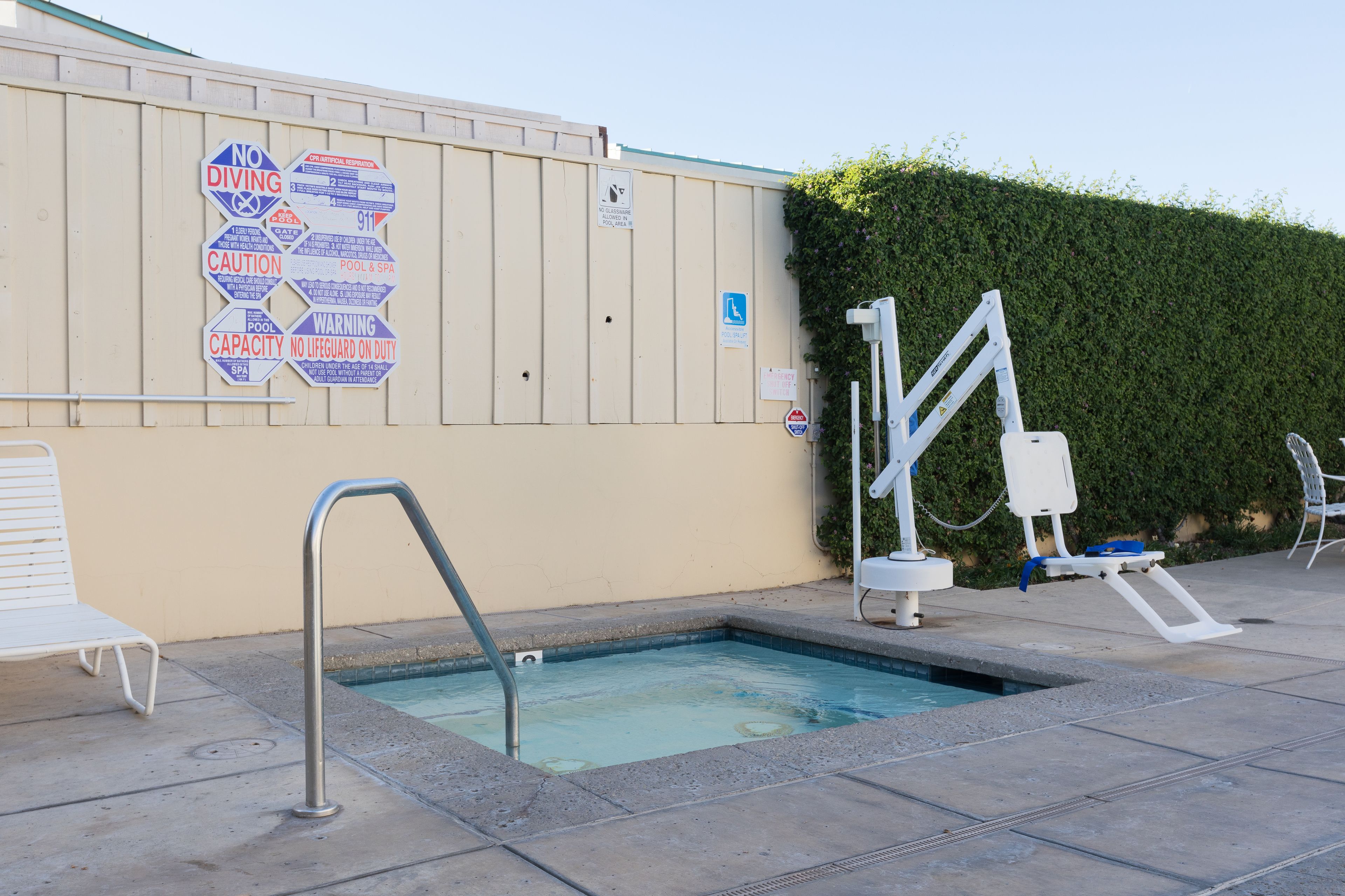Una piscina con un cartel de prohibido bucear, un puesto de socorrista y un letrero que indica la capacidad de la piscina.