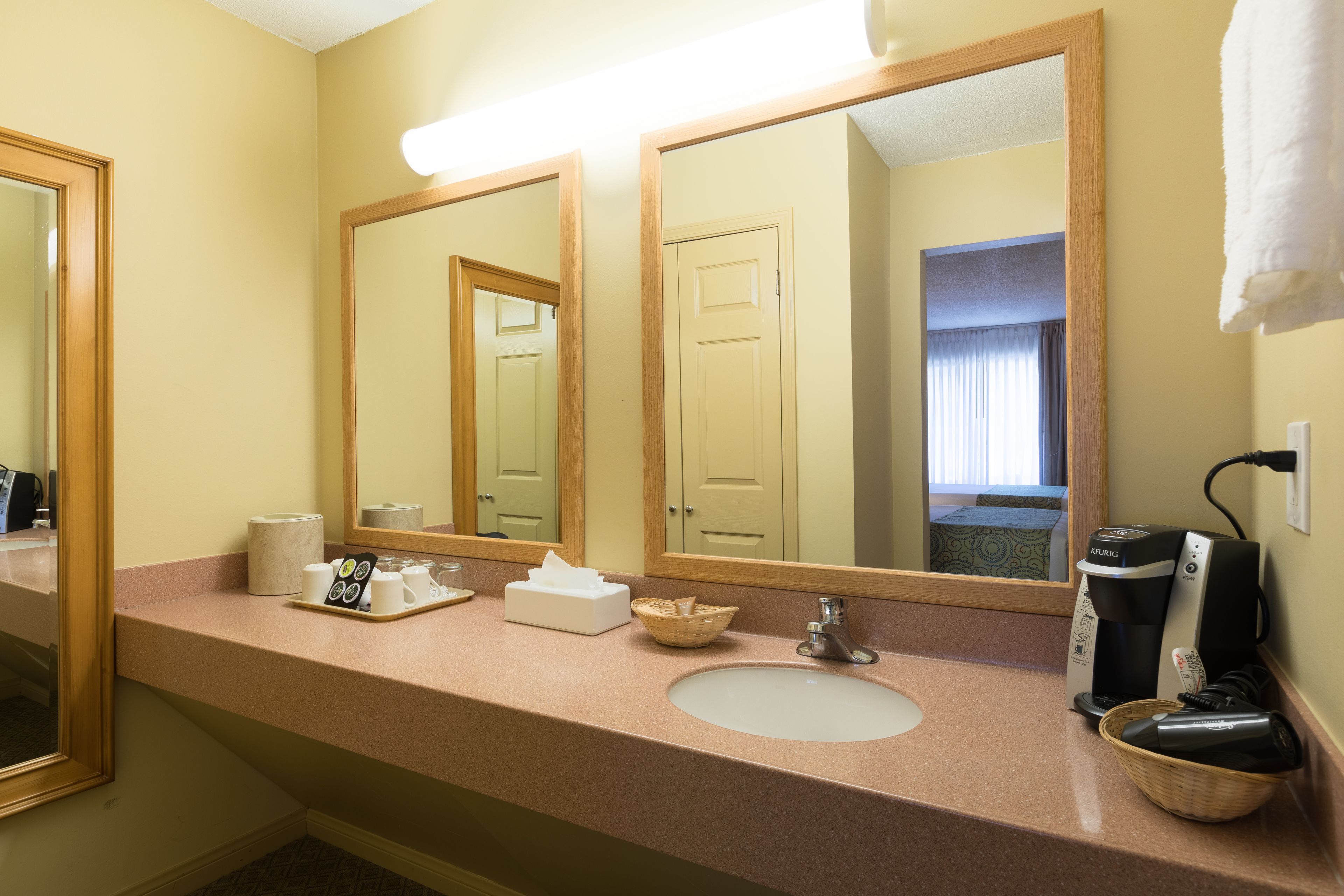Une salle de bain d’hôtel équipée d’un lavabo, de miroirs, d’une machine à café et d’un panier.
