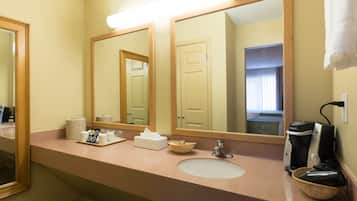 A hotel bathroom with a sink, mirrors, a coffee maker, and a basket.