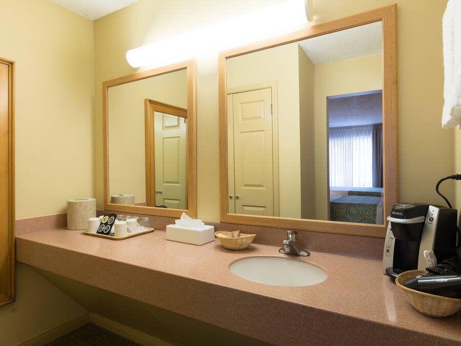 A hotel bathroom with a sink, mirrors, a coffee maker, and a basket.