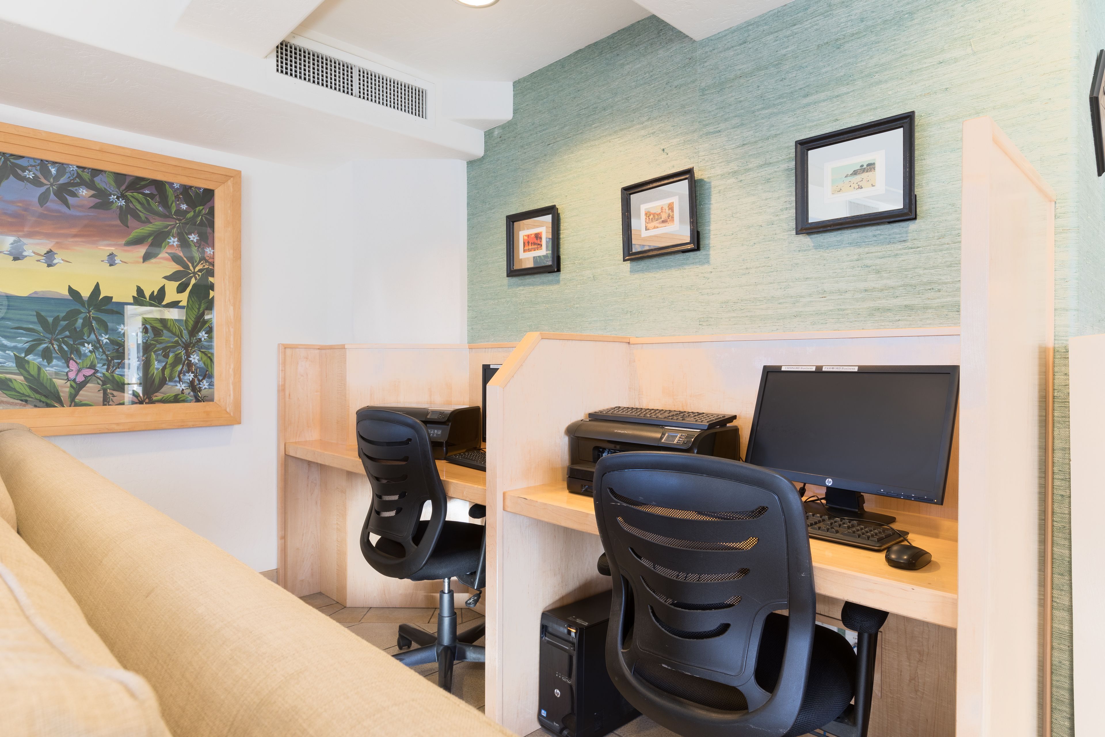 A workspace with two desks, each with a computer and printer, and a large painting on the wall.