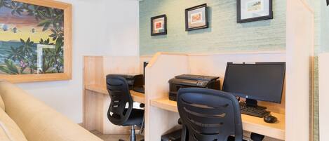 A workspace with two desks, each with a computer and printer, and a large painting on the wall.