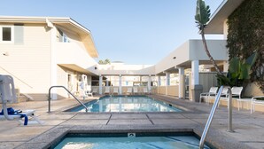 Uma piscina com deck ladrilhado, espreguiçadeiras e uma palmeira.