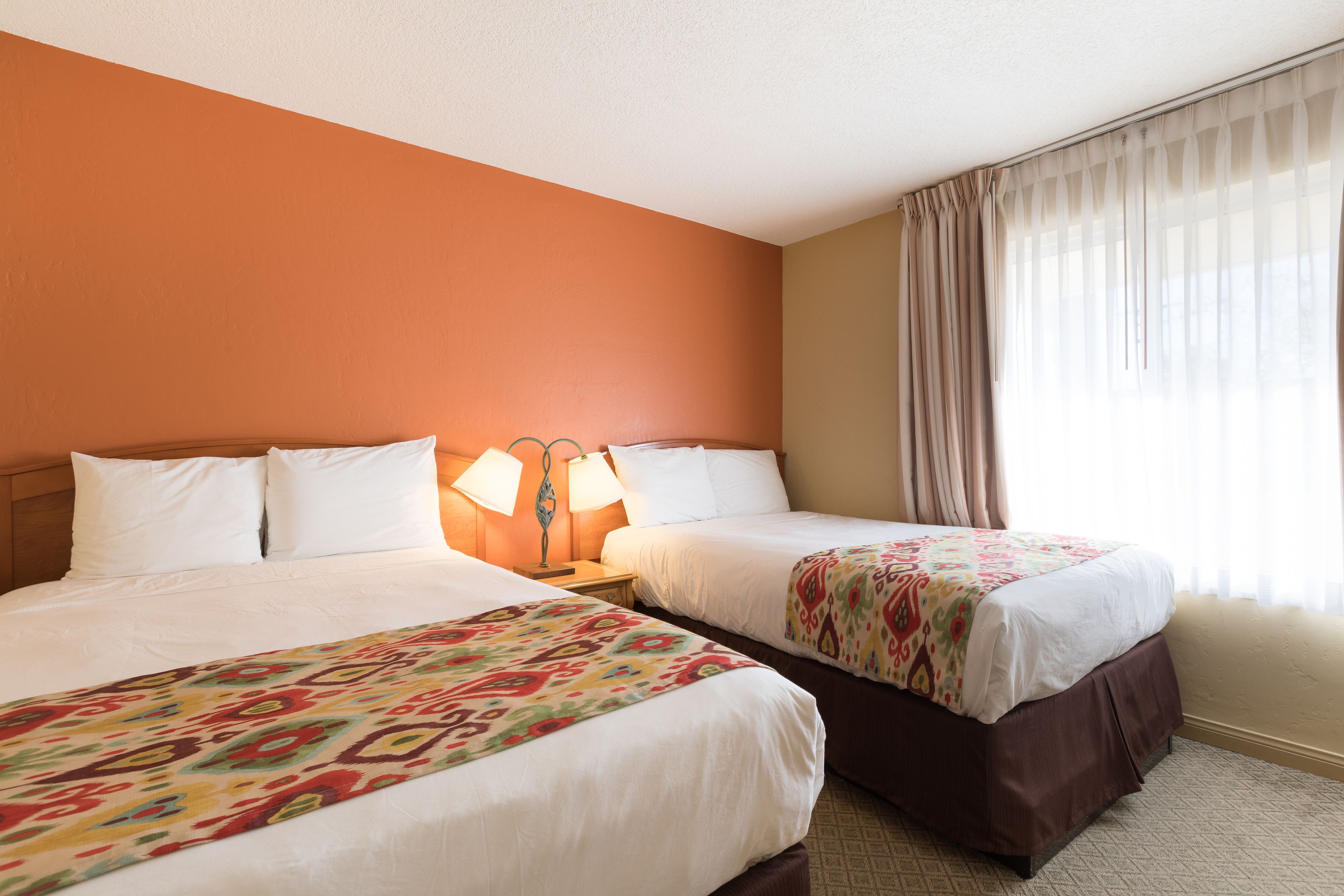 Una habitación de hotel con dos camas, una mesita de noche con lámparas y una ventana con cortinas.