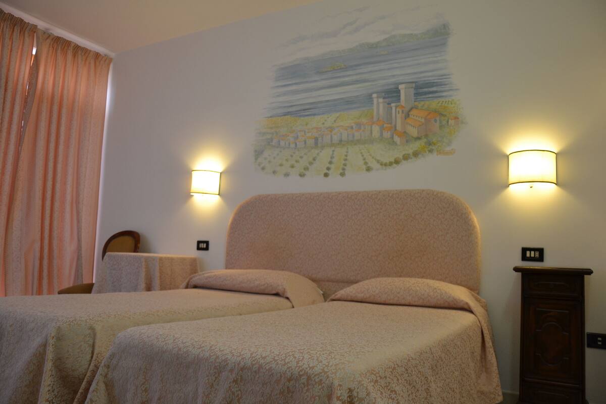 A hotel room with two beds, a mural on the wall, and two wall-mounted lamps.
