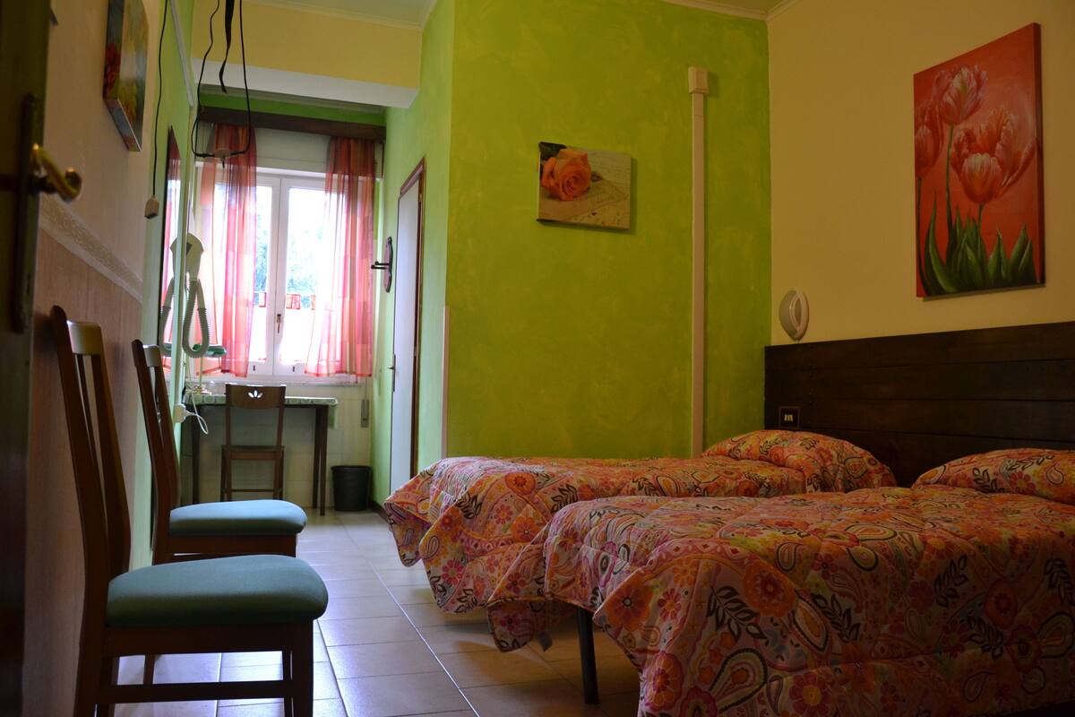 A room with two beds, a dining table, chairs, and a window with curtains.