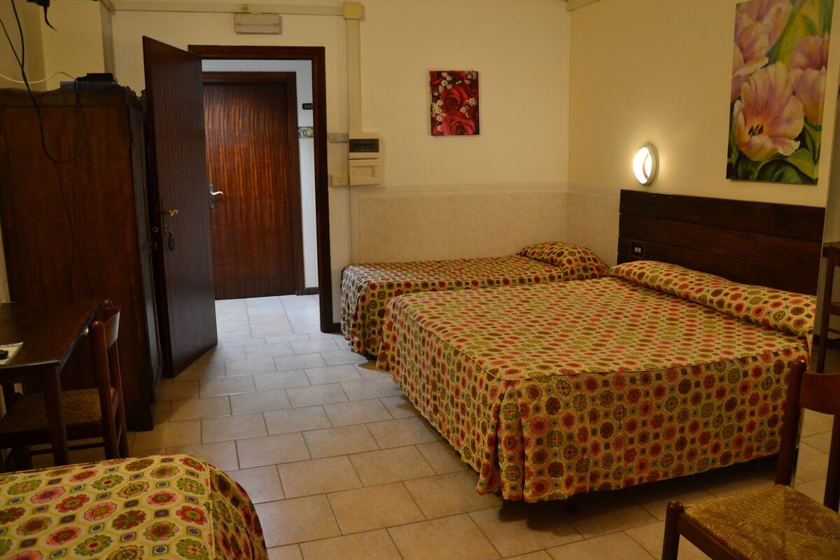 A hotel room with two single beds, a wooden wardrobe, a desk, and a chair.