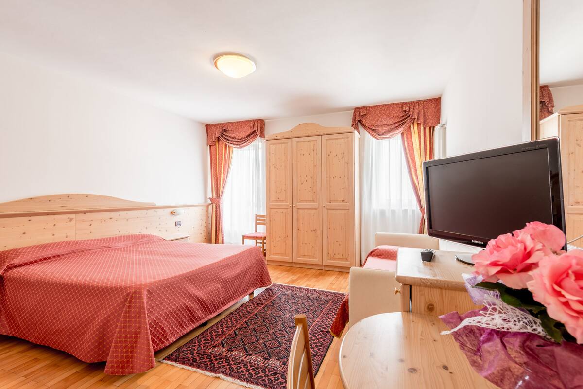 A bedroom with a bed, a TV, a desk, and a chair.