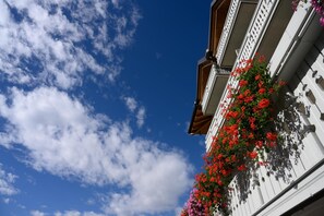 Un edificio con fachada blanca y balcón con flores rojas.