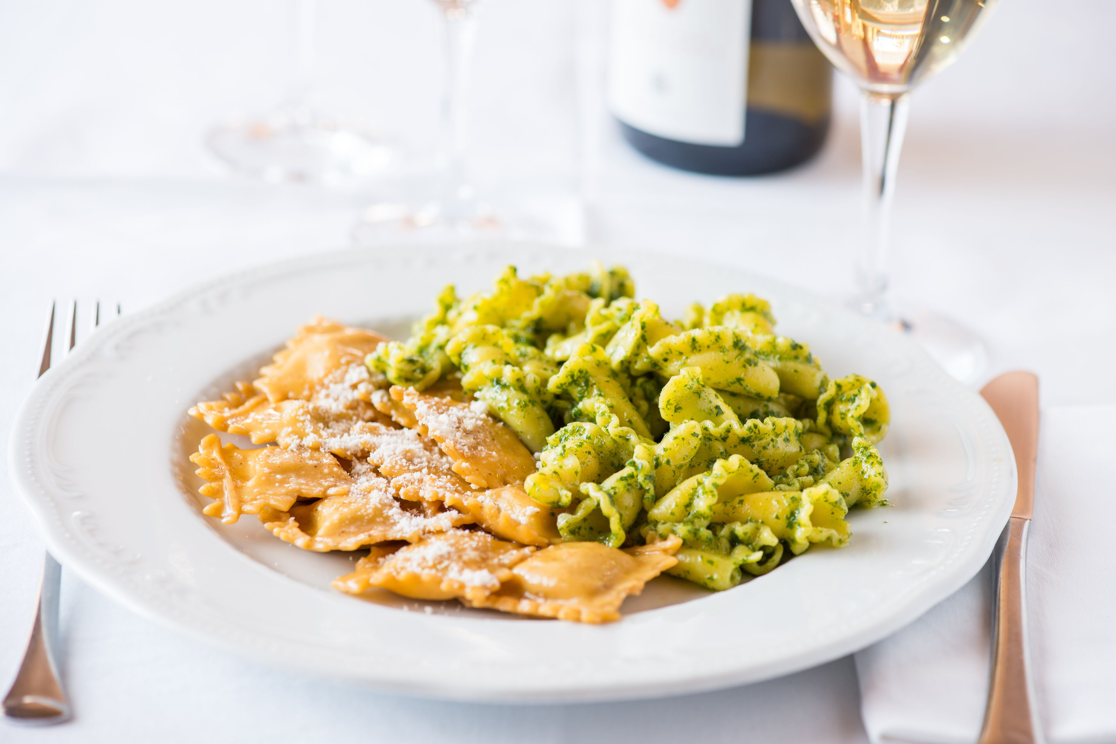 En tallerken pasta med grøn sauce og revet ost, serveret med et glas hvidvin.