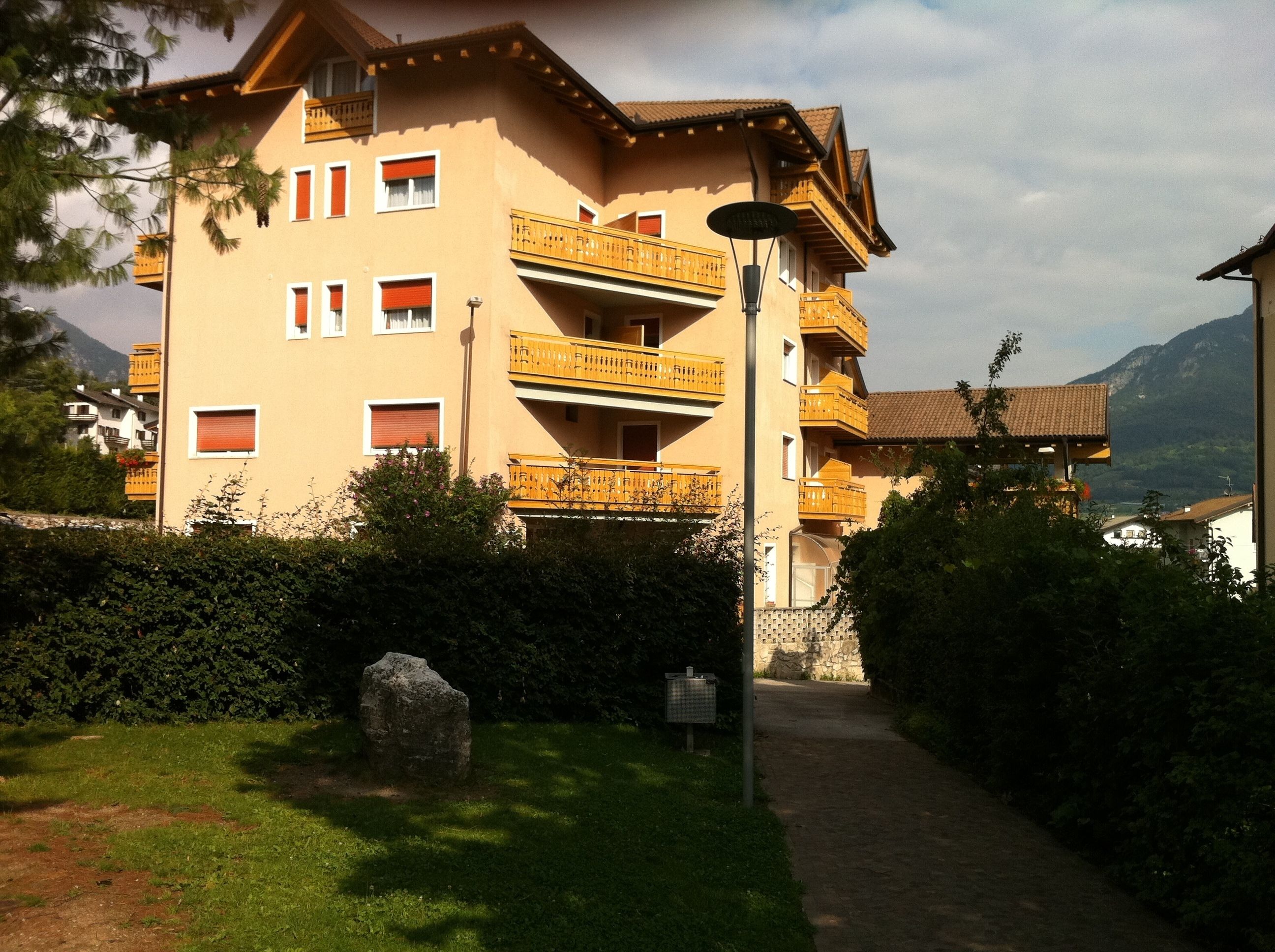 A multi-story building with balconies, a pathway leading to the entrance, and a mountainous backdrop.