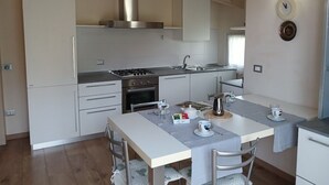 A compact kitchen with white cabinets, a gas stove, and a sink. There is a dining table with chairs and a small breakfast setup.