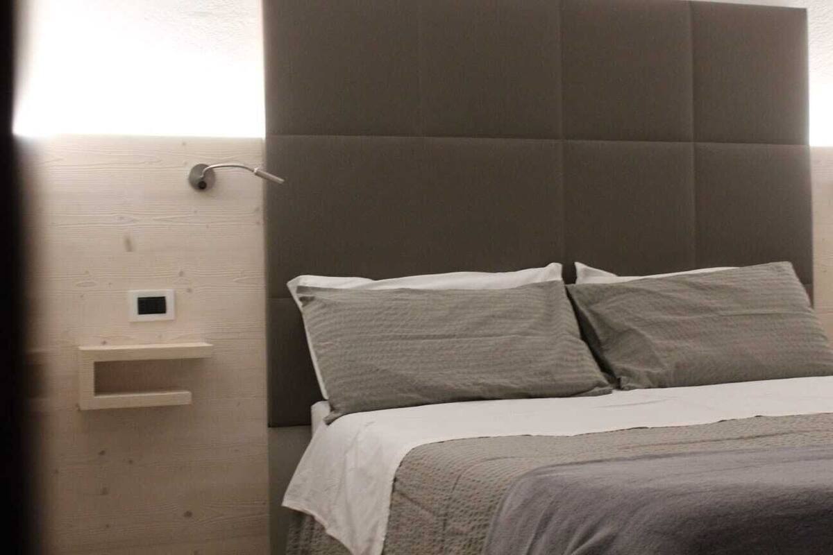 A bedroom with a bed, pillows, a nightstand, and a wall-mounted light fixture.