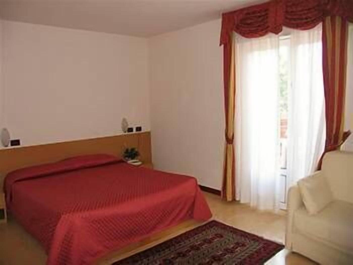 Quarto de hotel com cama, mesinhas de cabeceira, uma cadeira e janela com cortinas.