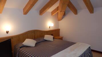A bedroom with a wooden ceiling, a bed with striped bedding, and two wall-mounted lights.