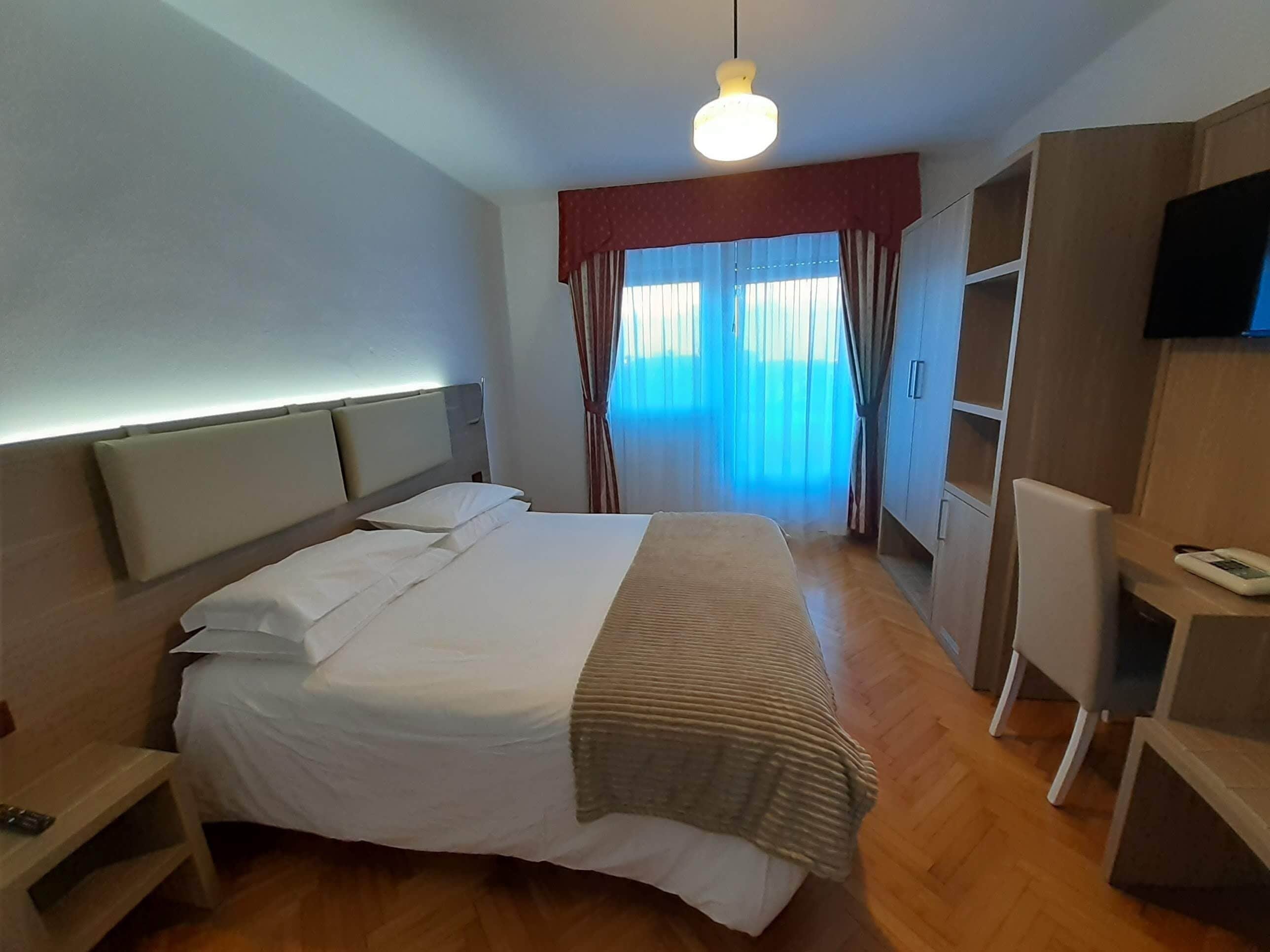 A hotel room with a bed, bedside table, wardrobe, and a TV.