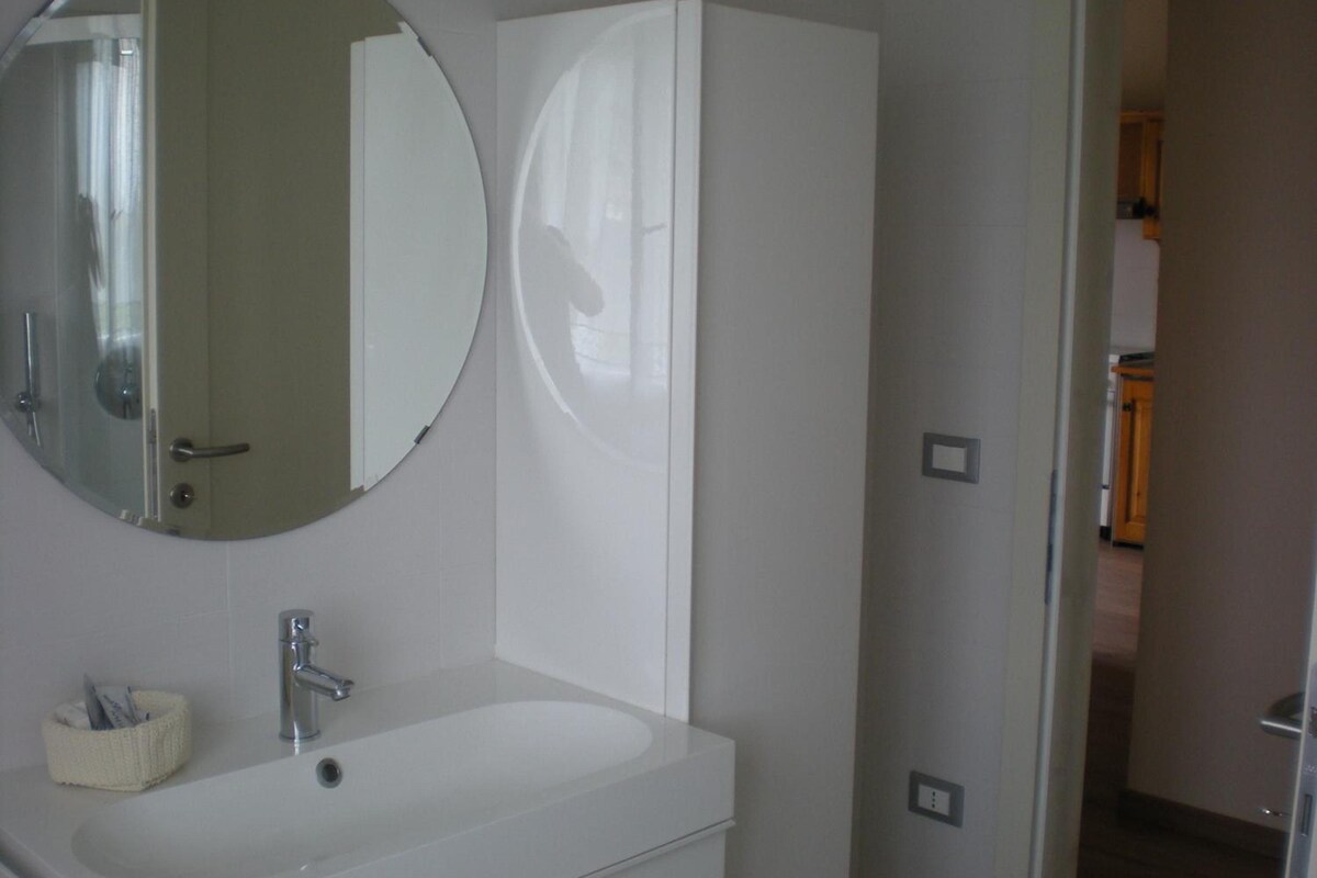 A bathroom with a round mirror, a white sink, and a cabinet.