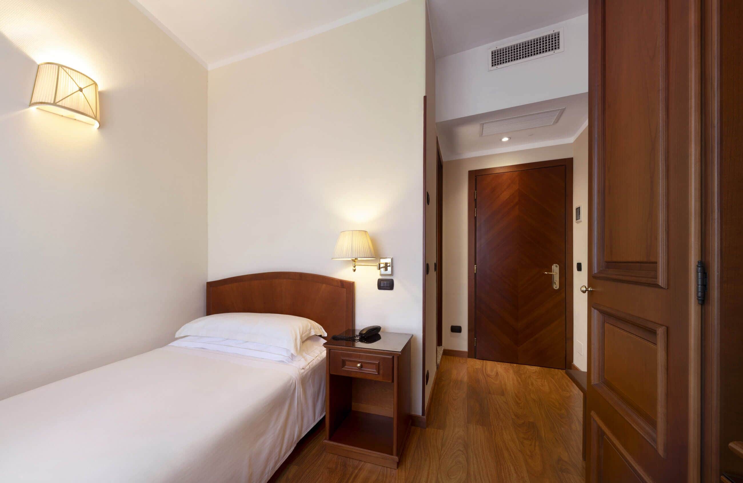 A hotel room with a bed, bedside lamp, nightstand, and a wooden door.