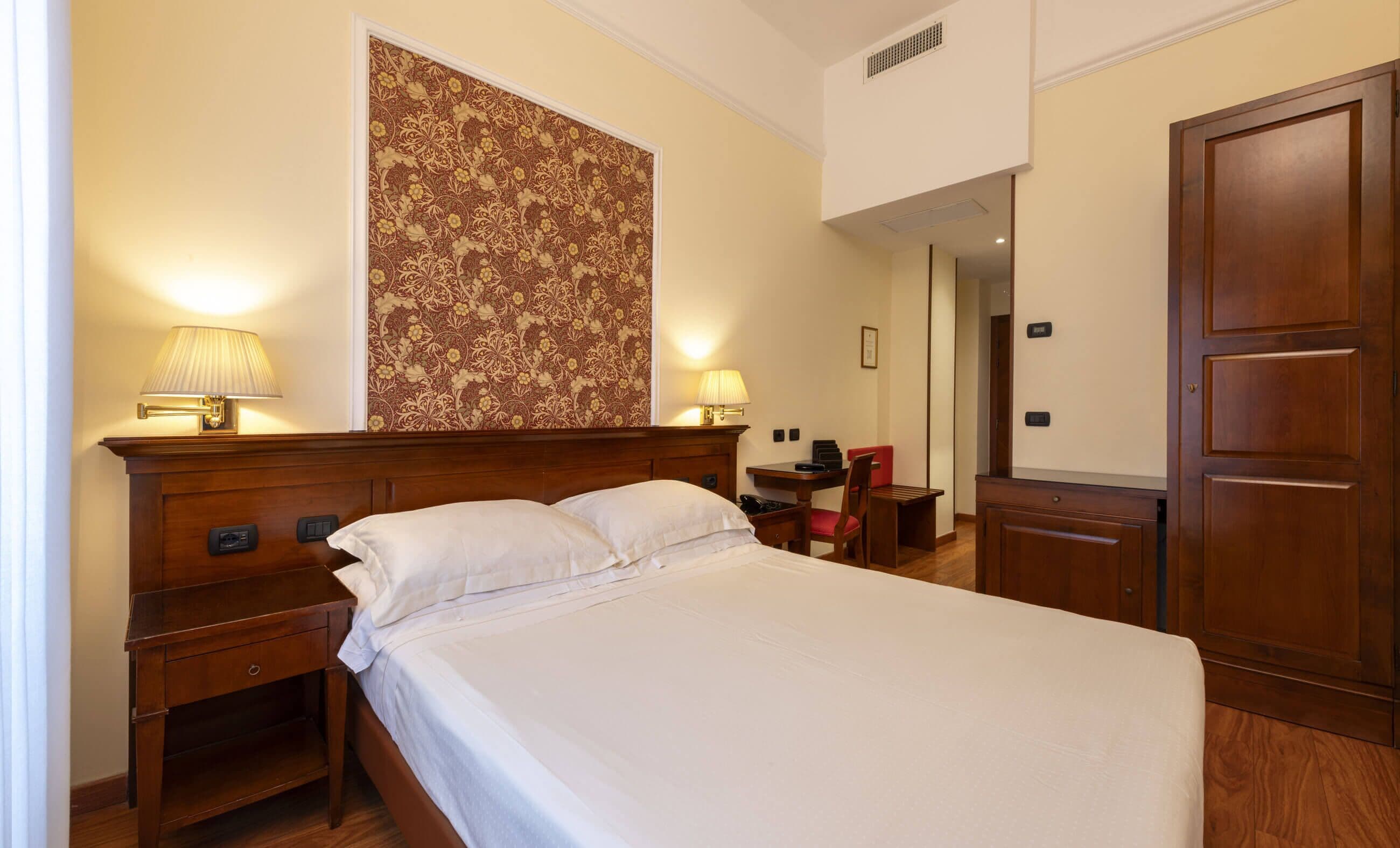Habitación de hotel con una cama grande, dos mesitas de noche con lámparas, un escritorio con silla y un armario.