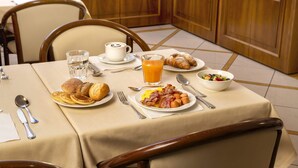 A breakfast table set with croissants, pancakes, bacon, eggs, and a fruit bowl. - Lancaster Hotel (Milan)