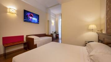 A hotel room with two beds, a desk, a chair, and a television displaying 'EURONEWS'.
