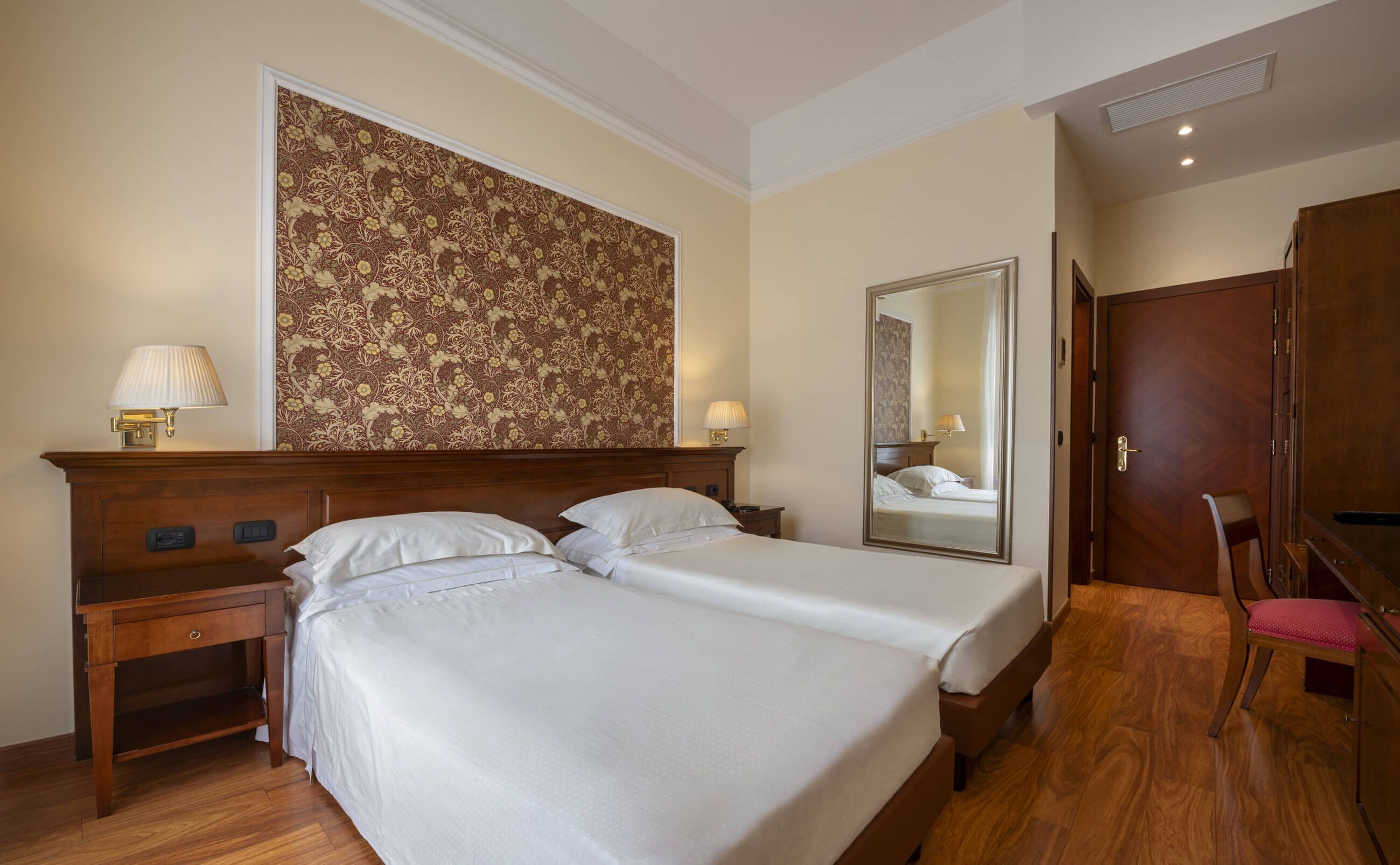 Ein Hotelzimmer mit einem großen Bett, zwei Nachttischen, einem Spiegel, einem Holzschrank und einem Sessel.