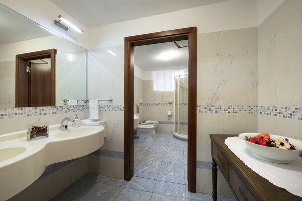 A modern bathroom with a large mirror, two sinks, a shower, and a toilet.