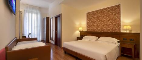 A hotel room with two beds, a TV, a desk, and a patterned wall.