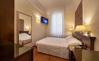 Een hotelkamer met een bed, televisie, spiegel en raam met gordijnen.