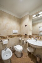 Ένα μπάνιο με μπιτέ, τουαλέτα, νιπτήρα και καθρέφτη.