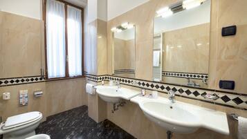 Een badkamer met drie wastafels, een toilet en een bidet.