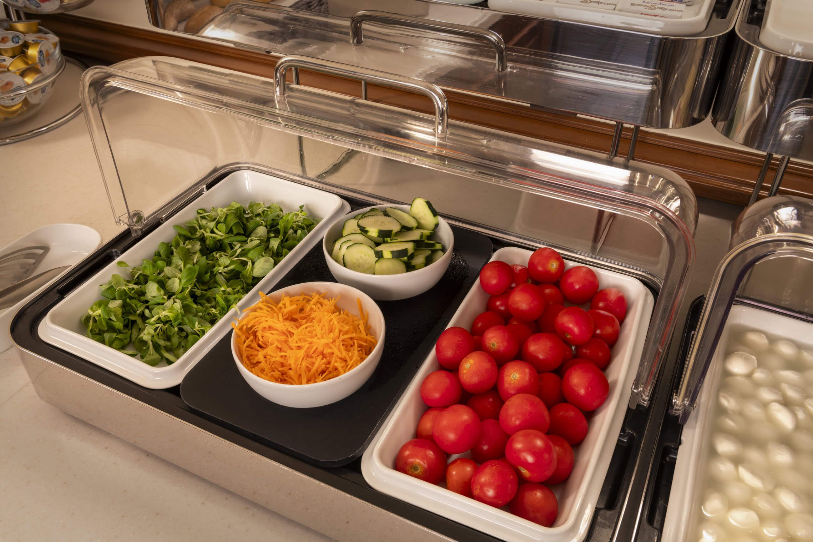 Un buffet proposant une variété d’aliments, notamment des légumes verts, du fromage râpé, des concombres et des tomates.