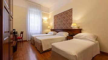Ein Hotelzimmer mit zwei Betten, Holzboden, Schreibtisch mit Stuhl, einer Lampe und einer großen Wand mit einem Blumenmuster.