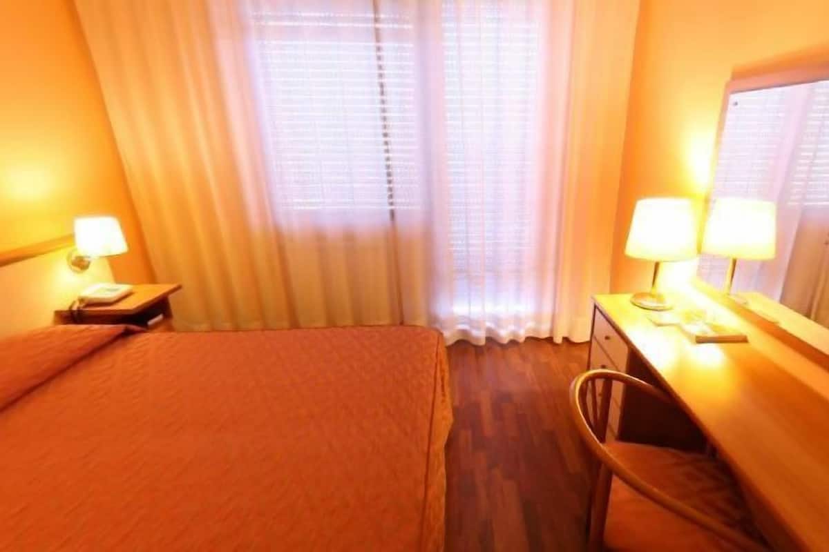 Une chambre d’hôtel comprenant un lit, un bureau avec une chaise, un miroir et deux lampes de chevet.