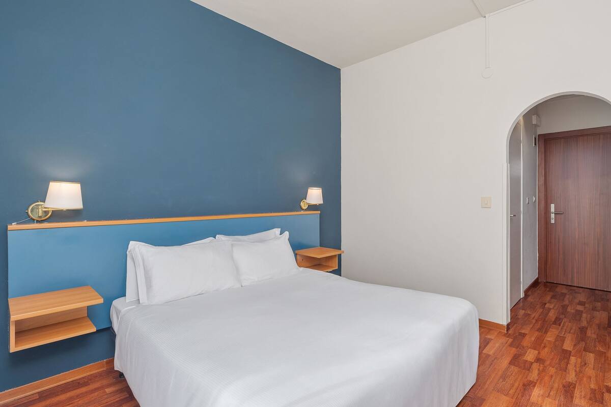 Une chambre à coucher avec un lit, deux lampes de chevet, une table de chevet en bois et un mur d’accent bleu.